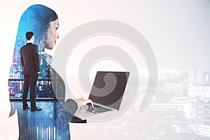 Thoughtful young female worker using laptop while standing on abstract white city background with forex chart and mockup place.