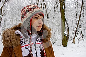 Thoughtful young girl in knitted cozy wear in snowy winter forest. Winter weather and clothes concept. Christmas background.