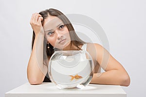 Thoughtful young girl looking at goldfish in a fishbowl