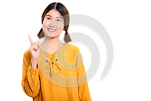 Thoughtful young happy Asian woman smiling while pointing finger