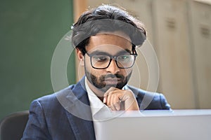 Thoughtful young indian business man analyzing market data, looking at computer.
