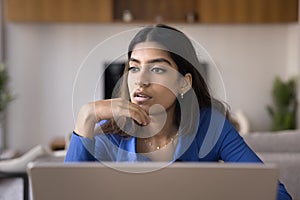 Thoughtful young Indian freelance entrepreneur woman working at laptop