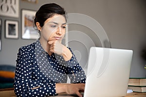 Thoughtful young indian woman looking at computer screen.