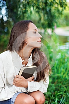 Thoughtful Young lady with book near the river