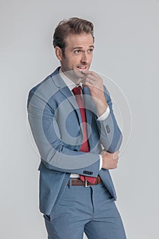 Thoughtful young man in blue suit holding hand to chin and thinking