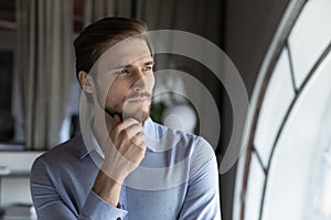 Thoughtful young man leader looking at window visualizing business opportunities