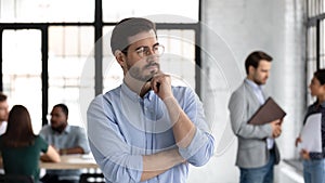 Thoughtful young man leader standing pondering in office workspace