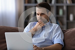 Thoughtful young man looking at laptop screen.