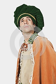 Thoughtful young man in old-fashioned costume with hands on hips against gray background