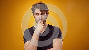 Thoughtful young man pondering something, touching his chin, yellow background