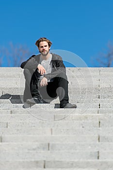 Thoughtful young man sitting on steps against blue sky background