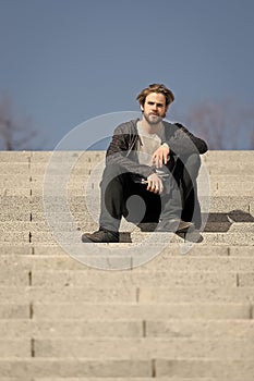 Thoughtful young man sitting on steps against blue sky background