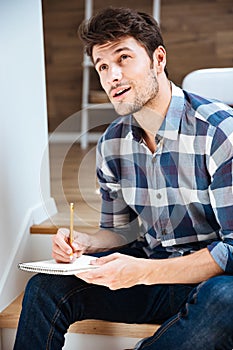 Thoughtful young man thinking and writing in notepad at home