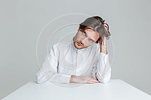 Thoughtful young man in white shirt sitting at the table