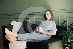 A thoughtful young middle-aged woman enjoying a rest and a cup of tea on the couch, pondering, looking at the open space