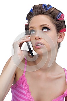 Thoughtful young model wearing hair rollers with phone