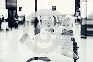 Thoughtful young mother looking trough window holding his infant baby boy child while waiting to board an airplane at