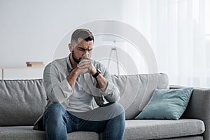 Thoughtful young serious handsome man sit on sofa at home, lost in thoughts, thinking about problem solving