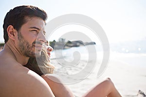 Thoughtful young shirtless man with his girlfriend sitting at beach