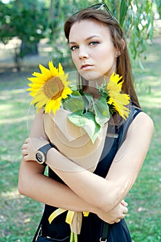 Thoughtful young woman in black dress holding sunflowers
