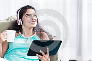 Thoughtful young woman holding coffee cup and digital tablet