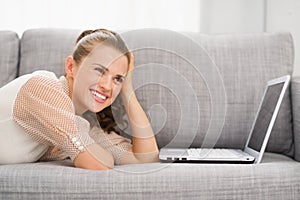 Thoughtful young woman laying on sofa with laptop