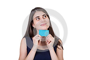 Thoughtful young woman looks dreamy aside while holding a blank gift card to her chin. Close up portrait of positive thinking girl