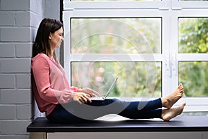 Thoughtful Young Woman Sitting On Floor Using Laptop