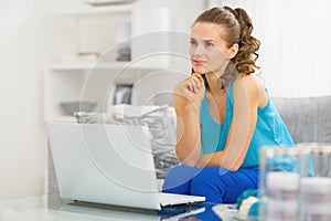 Thoughtful young woman sitting in living room and using laptop