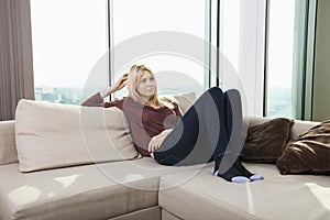 Thoughtful young woman sitting on sofa against window at home photo