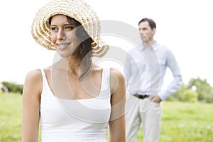 Thoughtful young woman smiling while man standing in background at park