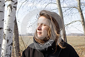 Thoughtful young woman standing near the birch trees in wintertime