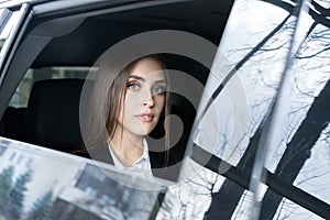 Thoughtful young woman in a suit sitting in the backseat of a car and looking through the window.