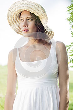 Thoughtful young woman in sundress and hat looking away in park