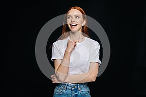 Thoughtful young woman in T-shirt and denim looking up empty space deep thinking on black background