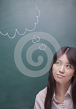 Thoughtful young woman with thought bubble on blackboard looking up