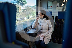 Thoughtful young woman travelling by train, dreamily looking out the window, enjoying her comfortable rail road trip