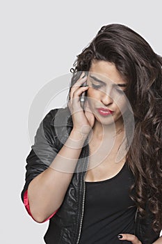 Thoughtful young woman using cell phone over gray background