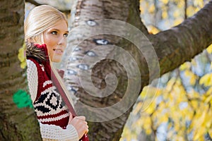 Thoughtful young woman in warm clothing standing near trees in park