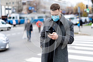 Thoughtfull man in mask standing near crossroad and searching in phone. Coronavirus pandemic in world.