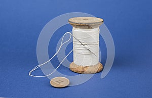 Thread on wooden reel with needle and button on blue.