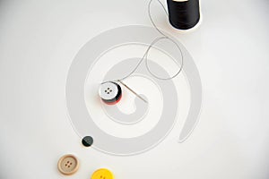 Threaded needle, buttons, and black spool of thread