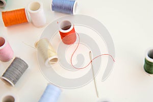 Threaded needle, red thread spool, and multi colored spools