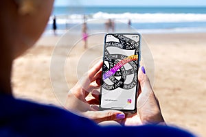 Threads app opening in a smartphone screen. Woman in the beach with a mobile phone in her hands. Text-based conversation