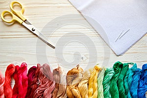 Threads, scissors, canvas and needles for embroidery on a  wooden surface.