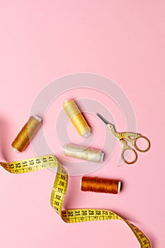 Threads, scissors and a measuring tape on a pink background