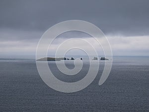 On a threatening and overcast grey day, the island of Gruney and the Ramna Stacks stacks off Mainland in Shetland, Scotland, UK