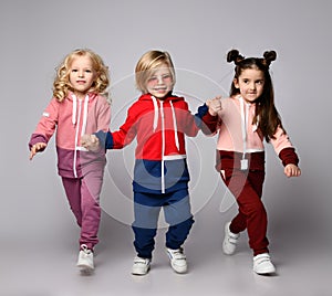 Three active kids two girls and a boy in modern sportswear run together holding hands.