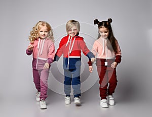 Three active kids two girls and a boy in modern sportswear are walking stepping forward together holding hands.