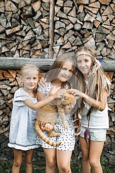 Three adorable happy little girls and a red cat outdoors. Kids and pets. Little girls hugging cute red cat standing near